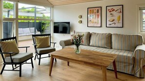 Ein modernes Wohnzimmer mit Holzboden, einer Couch, einem Couchtisch und einem an der Wand befestigten Fernseher.