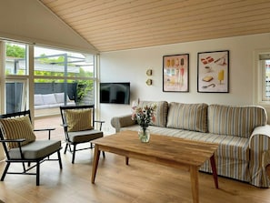 A modern living room with a wooden ceiling, a sofa, a coffee table, and a TV mounted on the wall. - Bright holiday home with large terrace near Nyborg (Nyborg)