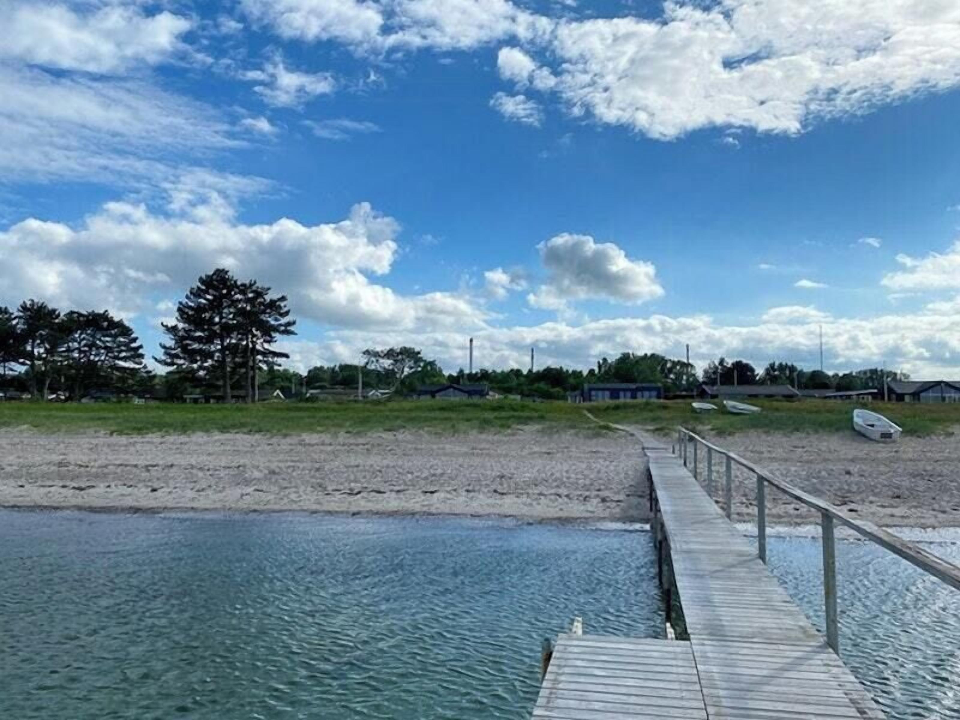 A wooden pier extending into a calm body of water, a sandy beach, and a row of boats.