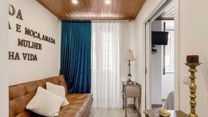 A living room with a brown leather sofa, a blue curtain, a small table with a lamp, and a decorative item on a console table. - Alfama The Best II, in Old Lisbon (Lisbon)