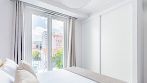 Ein Hotelzimmer mit Bett, Blick auf die Stadt durch ein großes Fenster und einem Balkon mit einem Stuhl.