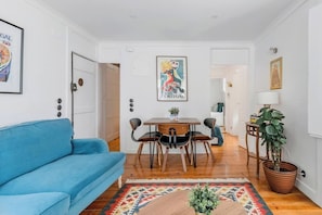 A living room with a blue sofa, a wooden dining table with chairs, a patterned rug, and a potted plant. - Vintage Inspired Flat in Lisbon (Lisbon)