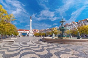 Ein Platz mit einem Brunnen, einer Statue und einem geometrisch gemusterten Pflaster.