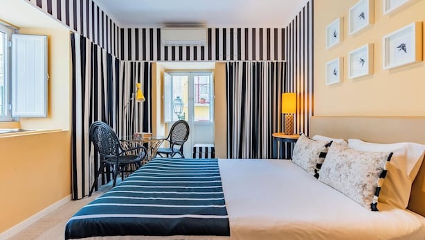 Hotellihuone, jossa on sänky, työpöytä, tuoleja, ikkuna ja ovi.
