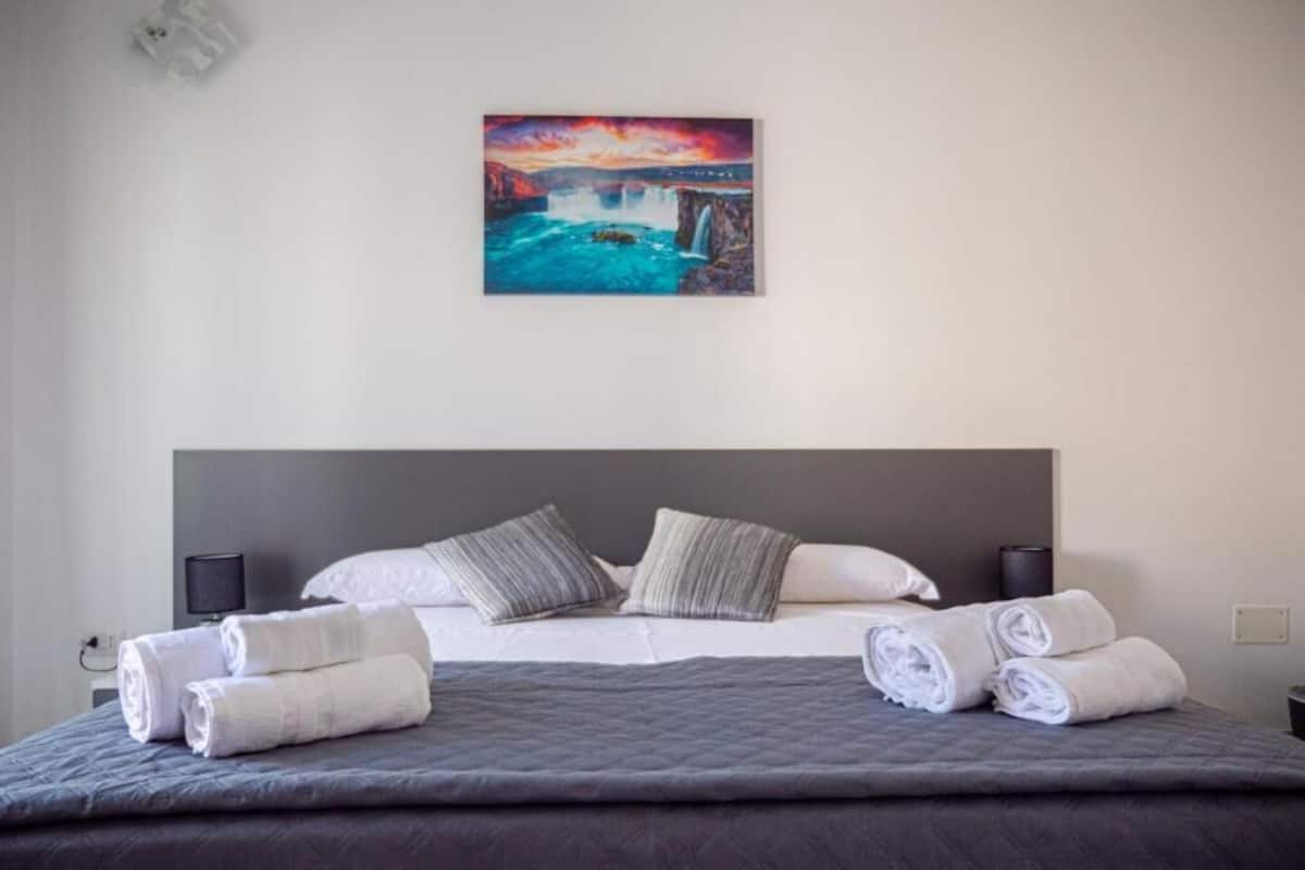A hotel room with a bed, pillows, a painting, and rolled towels.