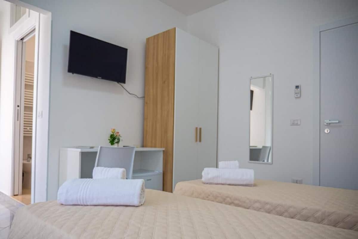 A hotel room with two beds, a TV, a wardrobe, a mirror, and a door.