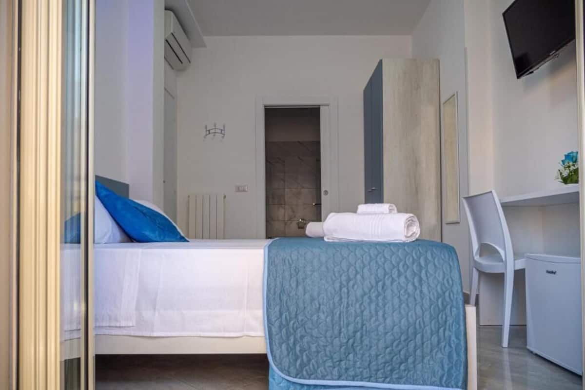 A bedroom with a bed, a desk, a chair, and a TV.