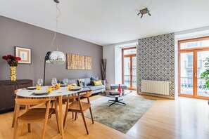A modern living room with a dining area, a sofa, a coffee table, and a large window with patterned curtains. - Chiado Mercy II With AC (Lisbon)