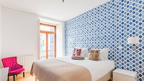 A bedroom with a large bed, a red chair, a white bedside table, and a patterned wall. - Chiado Mercy II With AC (Lisbon)