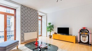 A living room with a glass coffee table, a sofa, a television, a jukebox, and a potted plant. - Chiado Mercy II With AC (Lisbon)