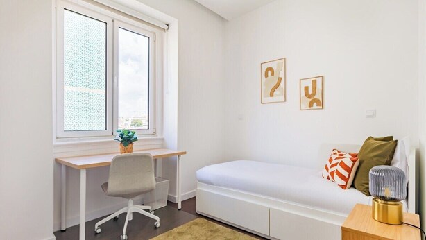Ein Zimmer mit Schreibtisch, Stuhl, Bett und Kunstwerken.