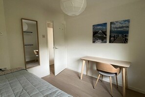 Ein Schlafzimmer mit einem Bett, einem Schreibtisch, einem Stuhl, einem Spiegel und zwei Wandbildern.