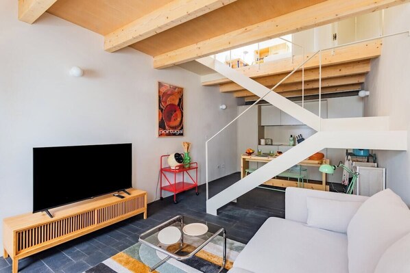 A modern living room with a flat-screen TV, a wooden console, a staircase, and a dining area. - Urban Pop Loft Alfama (Lisbon)