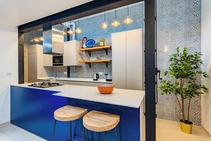 A modern kitchen with a blue island, wooden stools, hanging pendant lights, and patterned backsplash. - Stylish 2BR Apartment Ideal for Monthly Stays (Lisbon)