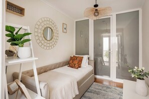 Ein Schlafzimmer mit Bett, einem Nachttisch mit Pflanze, einem Wandspiegel und einer Schiebeglastür, die auf einen Balkon führt.