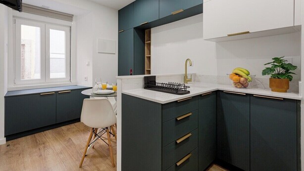 A modern kitchen with dark cabinets, a white countertop, a sink, and a window with blinds. - Petite Charm in Old Lisbon (Lisbon)