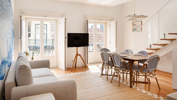 A living room with a sofa, a TV on a tripod, a dining table with chairs, and a staircase. - Baixa Rooftop Duplex Lisbon (Lisbon)