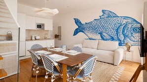 A modern kitchen with white cabinets, a microwave, and a dining area with striped chairs and a wooden table. - Baixa Rooftop Duplex Lisbon (Lisbon)