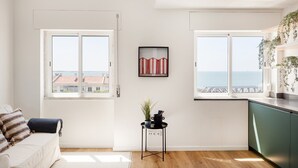 Een moderne woonkamer met een bank, een bijzettafeltje met een plant en twee grote ramen met uitzicht op zee.