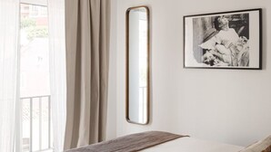 Een slaapkamer met een bed, een hanglamp, een lijst met een afbeelding en een raam met gordijnen.