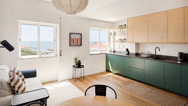 Een moderne keuken met groene kastjes, een zwarte spoelbak en een hangende lamp. Er zijn twee ramen met uitzicht op zee.