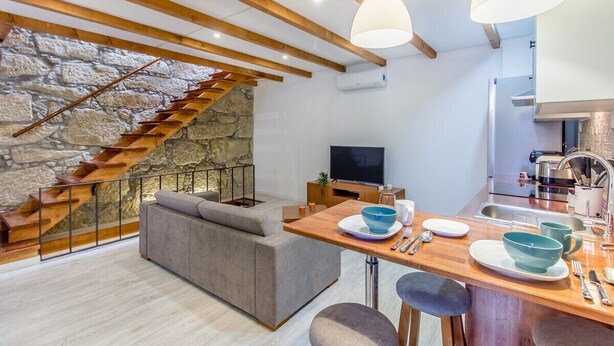 A modern interior with a stone staircase, a sofa, a dining area with a TV, and a kitchen. - Gaia Stone House (Vila Nova de Gaia)