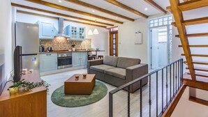 A modern kitchen with wooden beams, a dining area with a sofa, and a staircase. - Gaia Stone House (Vila Nova de Gaia)