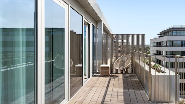 A modern balcony with glass doors, wicker furniture, and a view of the city. - Sal D'ouro Ocean Views Gym Garage (Vila Nova de Gaia)