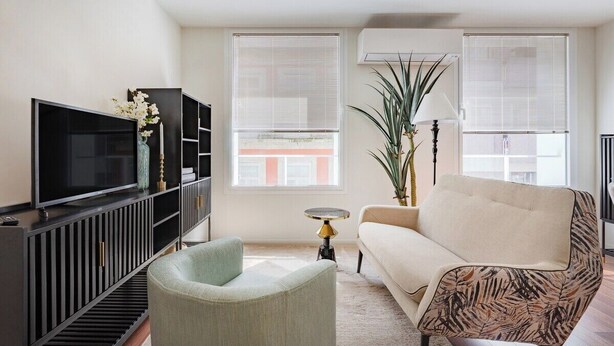 Ein Wohnzimmer mit Fernseher, Sofa, Sessel und Blumentopf.