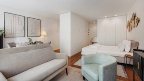 Ein modernes, minimalistisches Schlafzimmer mit Sofa, Sessel, Bett und Kleiderschrank.