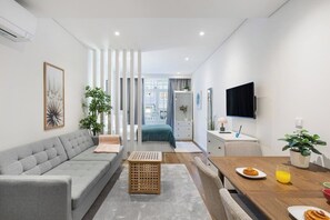 Ein modernes Wohnzimmer mit Sofa, Esstisch, Geschirr und einem Glas, einem Fernseher und Blick ins Schlafzimmer.