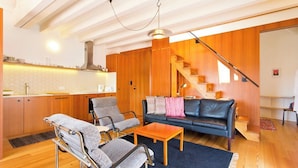 Een moderne woonkamer met een bank, twee fauteuils, een salontafel en een trap die naar een hoger gelegen verdieping leidt.