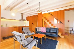 Ein modernes Wohnzimmer mit einer Couch, zwei Sesseln, einem Couchtisch und einer Treppe, die in eine andere Ebene führt.