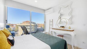 A modern hotel room with a large bed, a desk, and a balcony with a view.