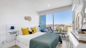 A modern bedroom with a bed, bedside table, lamp, and a view of the city through large windows. - Blue Breeze Espinho Pool View, Gym Balcony (Espinho)