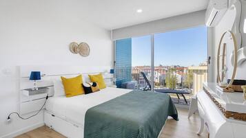 A modern bedroom with a bed, bedside table, lamp, and a view of the city through large windows.