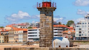 A lighthouse with a red top, a stone base, and a clear sky in the background. - Charming 3BR w/ Office Garage by Foz Beaches (Porto)