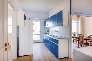 Eine kleine Küche mit blauen Schränken, einem weißen Kühlschrank und einem Essbereich mit Holzsesseln.