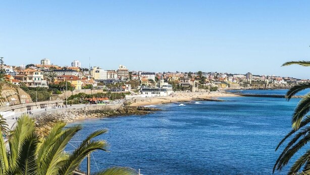 A coastal cityscape with a beach, buildings, and a clear blue sky. - Estoril Beach Your Family Escape (Cascais)
