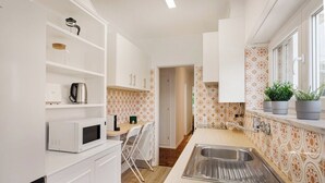 A kitchen with white cabinets, a microwave, a kettle, and a sink. - Estoril Beach Your Family Escape (Cascais)