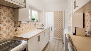 A narrow kitchen with patterned wallpaper, white cabinets, and a window. - Estoril Beach Your Family Escape (Cascais)