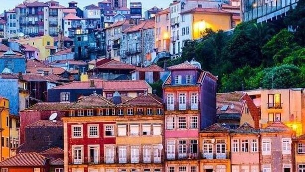 A waterfront cityscape with historic buildings, a prominent tower, and a river reflecting the lights. - Oasiys - Your Getaway in Porto (Porto)