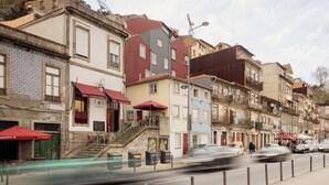 A row of multi-story buildings with balconies, a street with cars, and a pedestrian walkway. - Oasiys - Your Getaway in Porto (Porto)