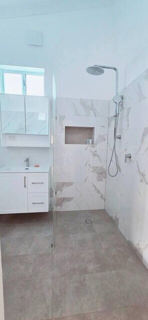 Un baño con ducha, tocador con espejo y ventana.