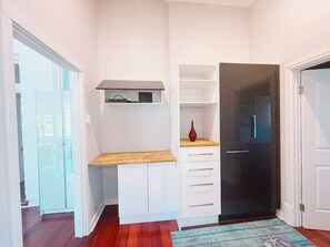 Una habitación compacta con escritorio integrado, armario y una puerta que da a otra habitación.