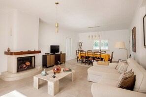 Ein Wohnzimmer mit Kamin, Sofa, Couchtisch, Fernseher, Essbereich und hängenden Lampen.