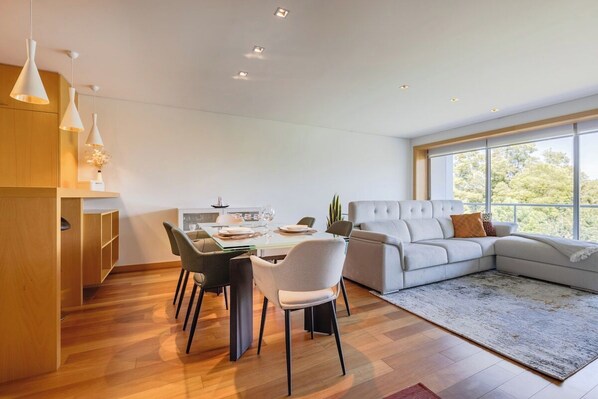A modern living room with a sectional sofa, dining table with chairs, and pendant lighting. - Gaia Prime Serenity (Vila Nova de Gaia)