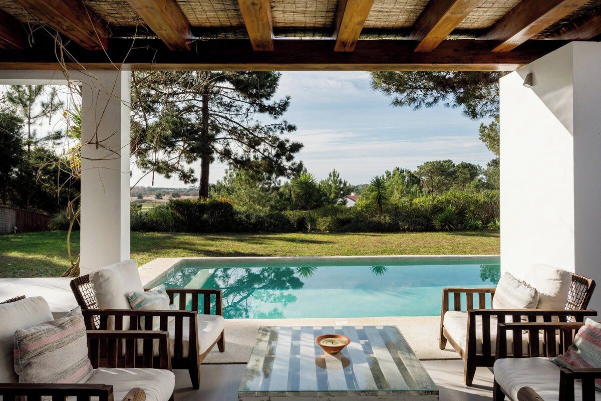 A poolside area with wooden furniture and a view of the pool and surrounding greenery.
