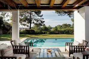 A poolside area with wooden furniture and a view of the pool and surrounding greenery. - Casa Glicinias in Comporta (Grandola)