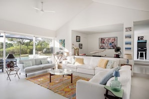A spacious living room with a white sofa, a coffee table, and a colorful rug. There is a large window providing a view of the outdoors. - Casa Glicinias in Comporta (Grandola)